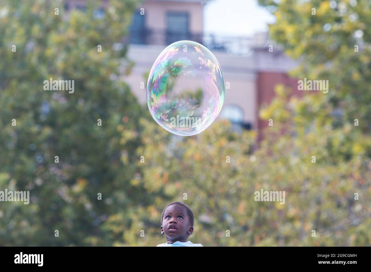 Suwanee, GA, USA - 21. September 2019: Ein kleiner Junge sieht erstaunt zu, wie eine eiförmige Blase auf seinem Kopf schwebt, bei einem Herbstfest. Stockfoto