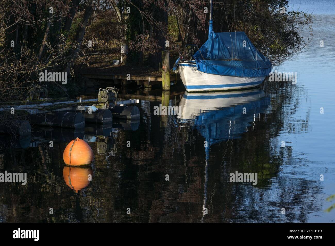 Überdachtes Segelboot mit blauer Plane und einer orangefarbenen Boje im See am Ufer, Freizeitangebot, Kopierraum, ausgewählter Fokus, enge Tiefe Stockfoto