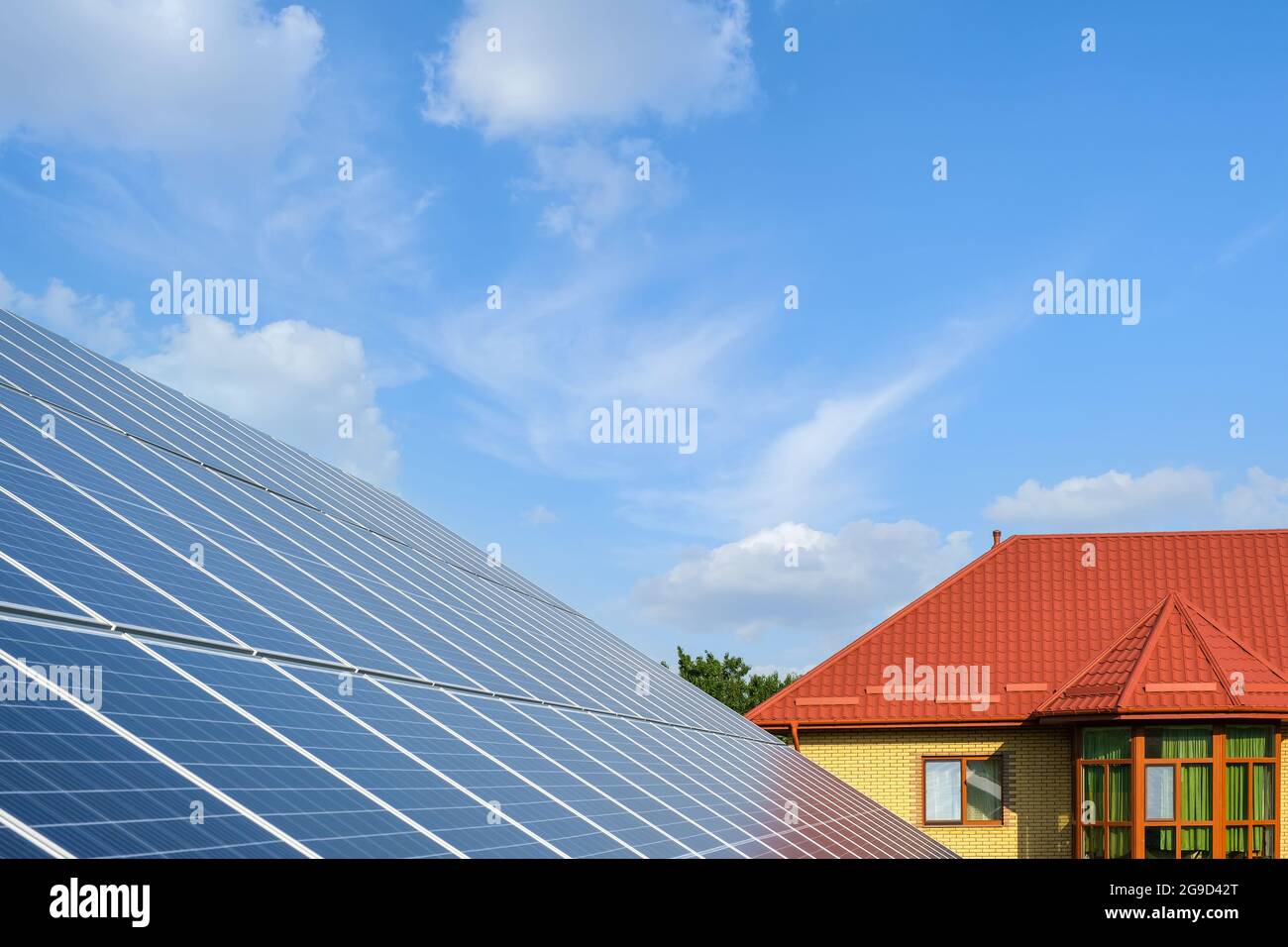 Reihe von Sonnenkollektoren auf einer Solarfarm und Haus unter einem blauen Himmel. Stockfoto