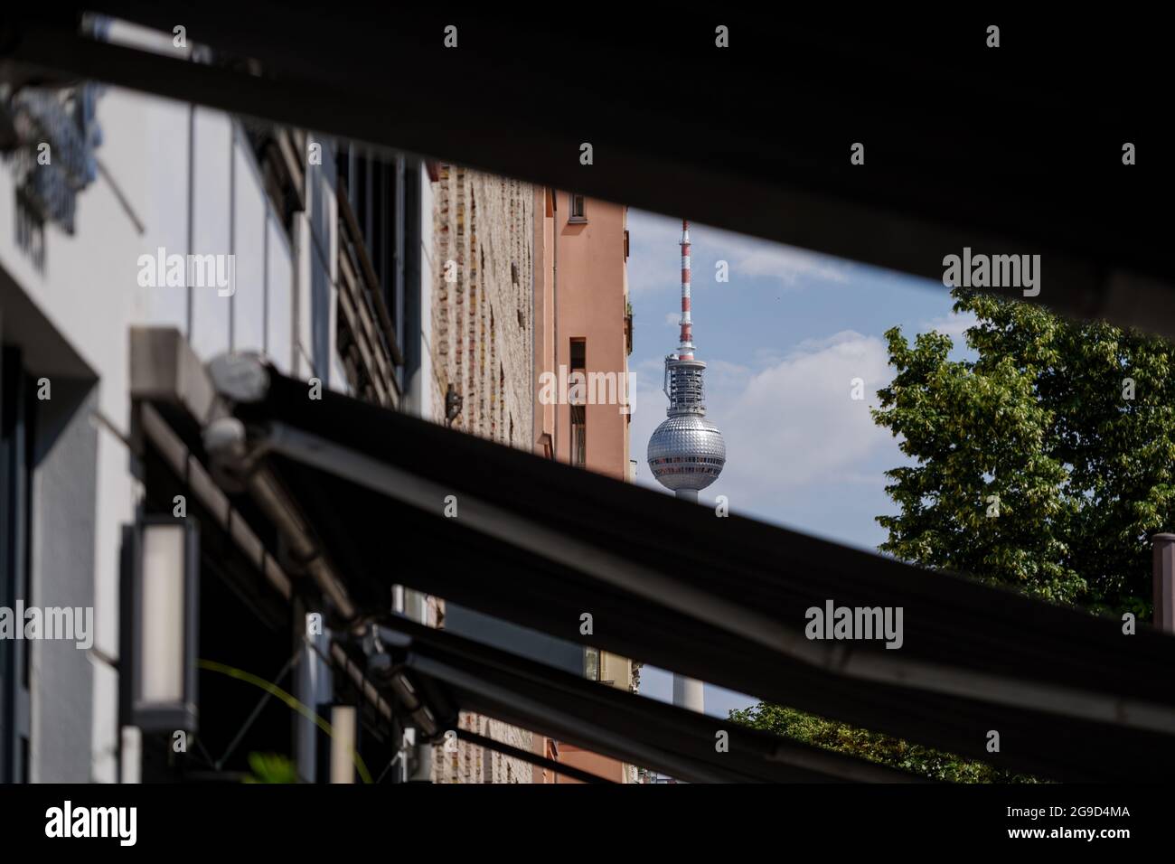 Selektiver Blick auf den Berliner Fernsehturm durch eine Lücke zwischen Markisensonnenschutz über Bürgersteig entlang der Straße in Berlin, Deutschland. Stockfoto