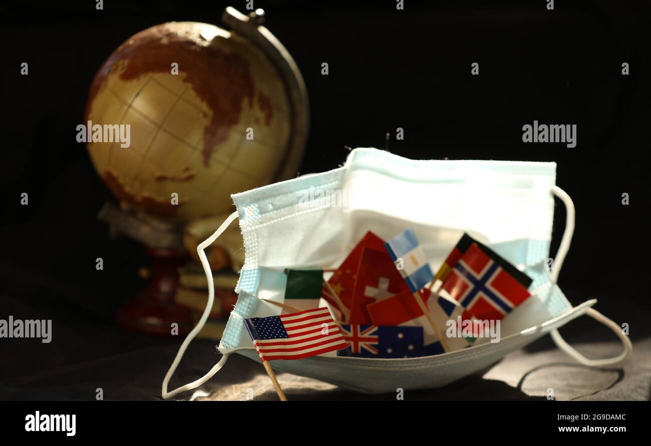 Eine Reihe von mehreren kleinen Nationalflaggen in einer offenen Covid-19 Gesichtsschutzmaske. Altmodischer Globus im Hintergrund. US-Flagge auffällig Stockfoto