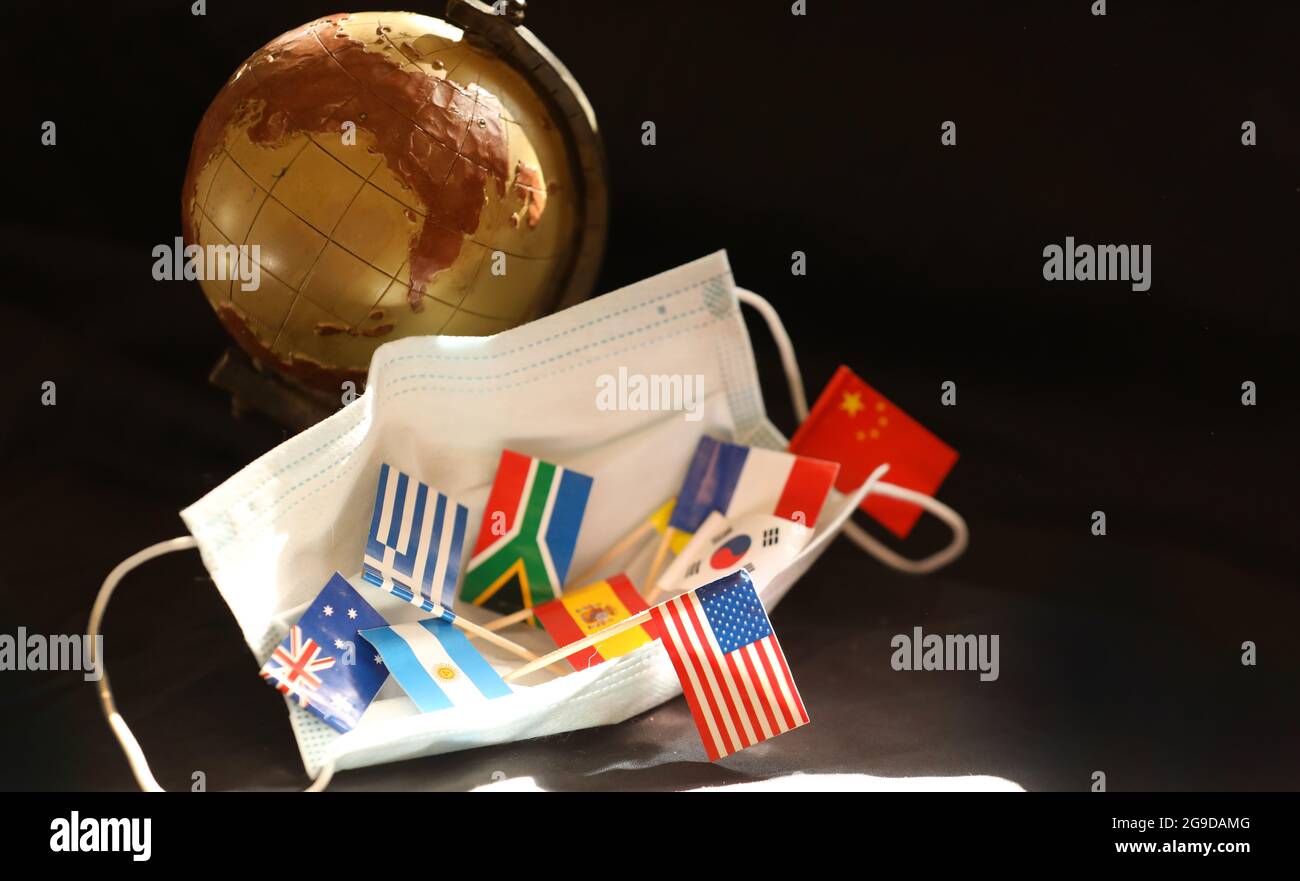 Mehrere kleine Nationalflaggen, die in einer offenen Coronavirus-Gesichtsmaske mit altmodischem Welt-Globus-Modell im Hintergrund ruhen. Stockfoto