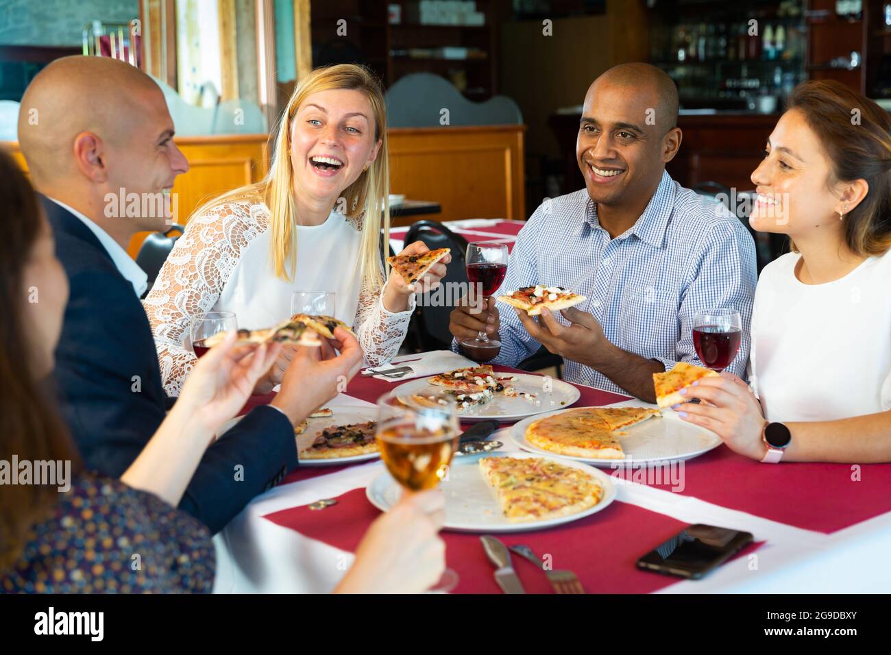 Glückliche Freunde essen leckere Pizza und plaudern miteinander im Restaurant Stockfoto