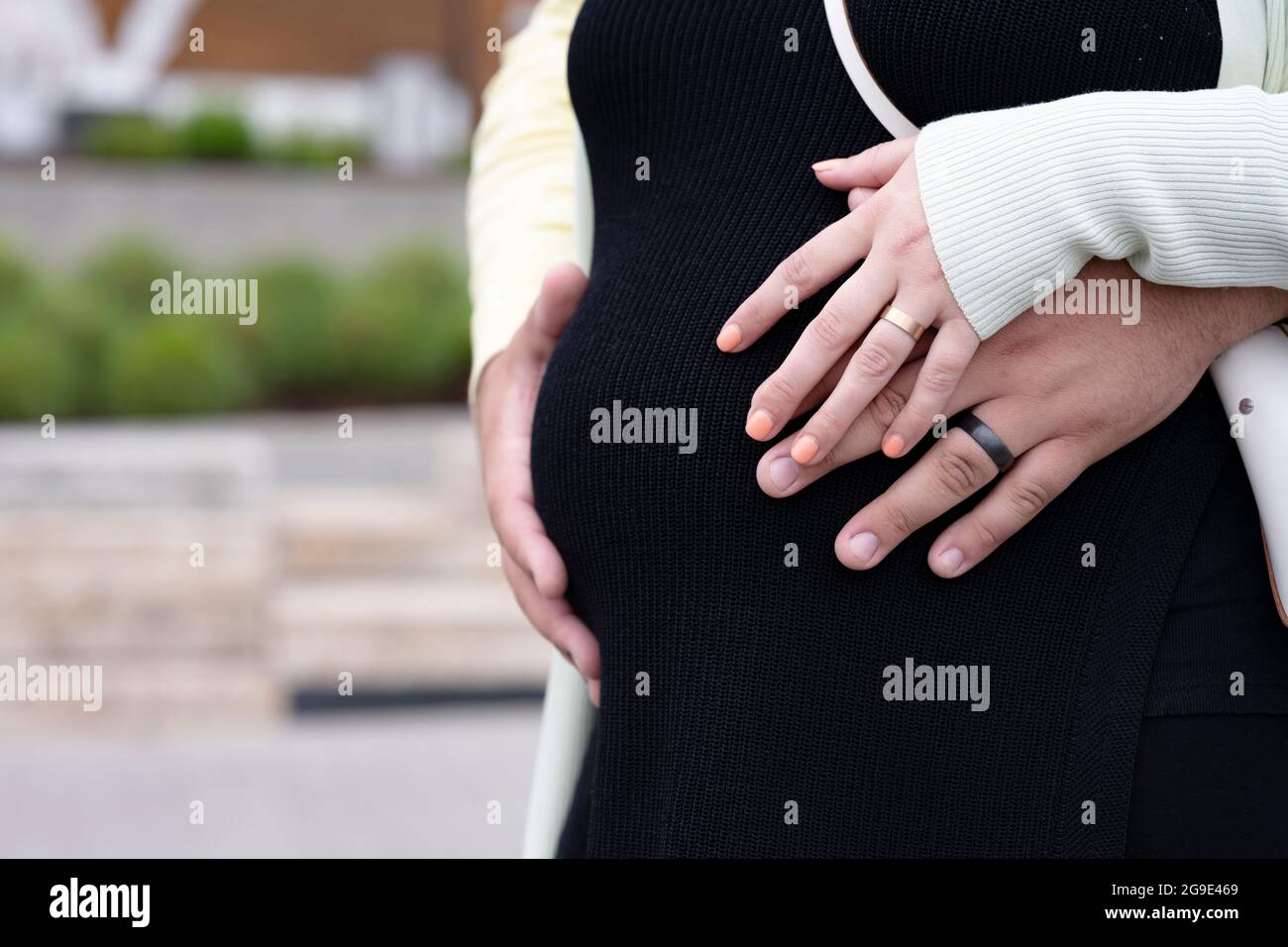 Zukünftige Eltern der Ehemann und die Ehefrau umarmen symbolisch die Hände des ungeborenen Kindes, das sich im Mutterleib ihrer Schwangeren befindet und zärtliche Gebühren ausdrückt Stockfoto