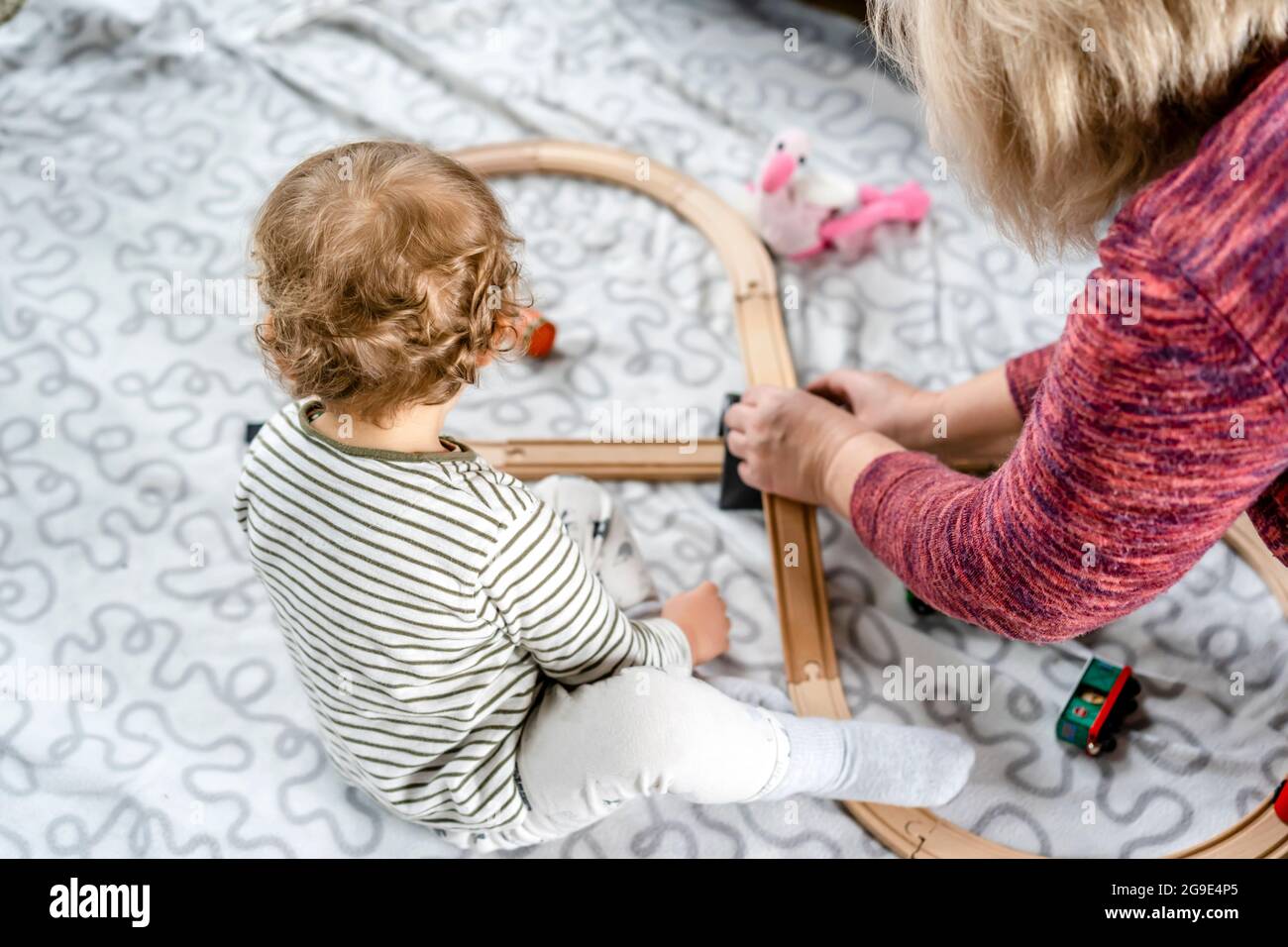 Die Oma spielt mit ihrem Enkeljungen mit Eisenbahnspielzeug und Autos auf dem Spielplatz und lehrt ihn mit Liebe, Fantasie zu nutzen und das reale Leben zu simulieren Stockfoto