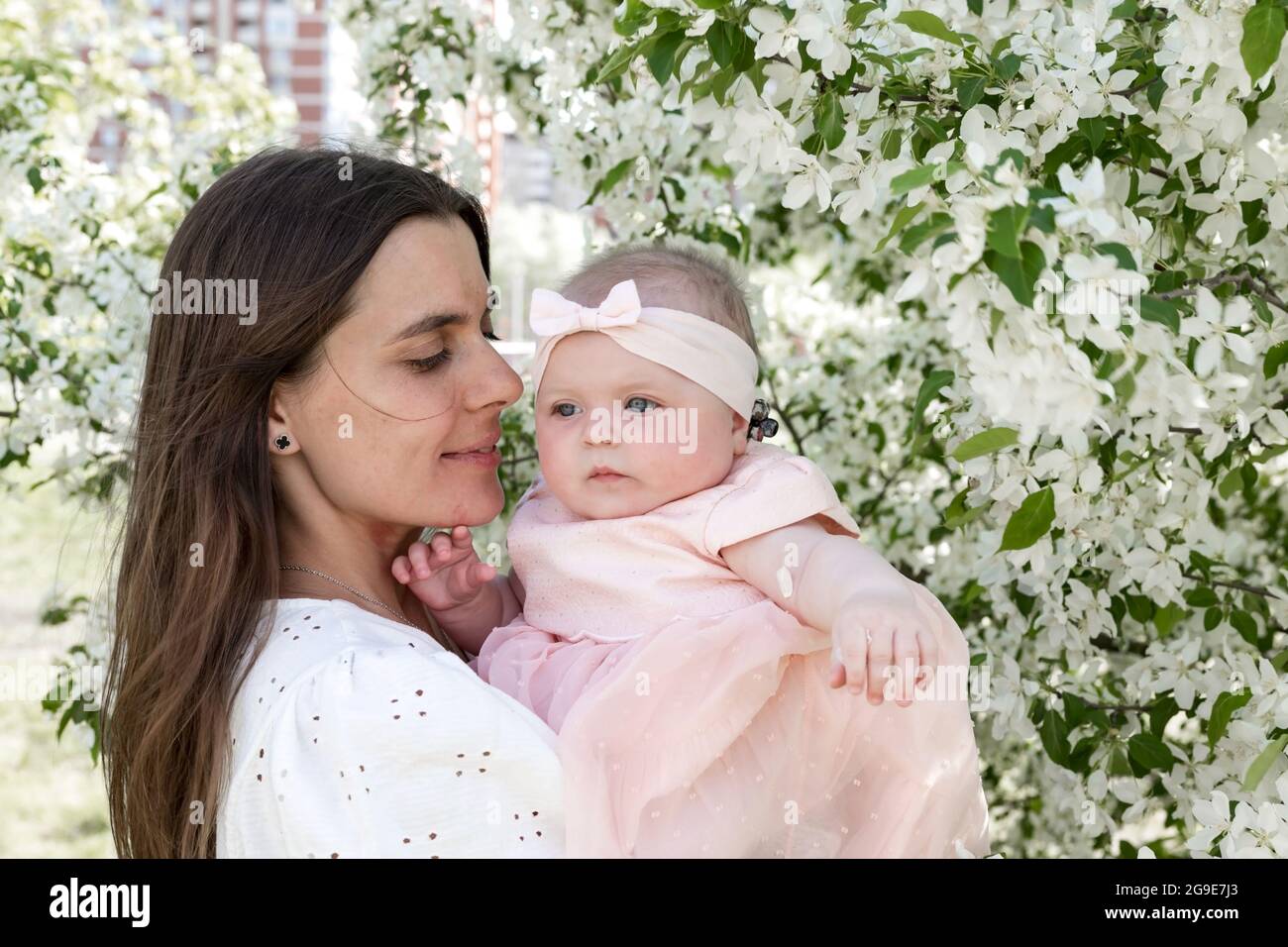 Lächelnde und attraktive Frau mit kleinem Kind. Nettes und kleines Mädchen in rosa Kleid. Schöne und hübsche Mutter in weißen Kleidern. Horizontale Aufnahme. Stockfoto