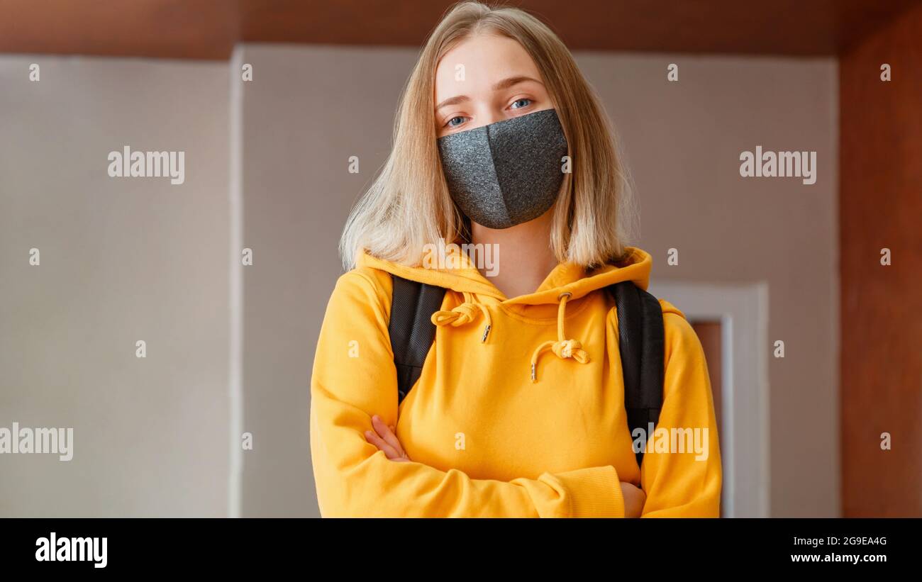 Student Mädchen mit Armen gekreuzt in der Universität im Inneren während Coronavirus covid Lockdow. Schulmädchen in Maske mit Rucksack. Junge Frau Studentin in Stockfoto