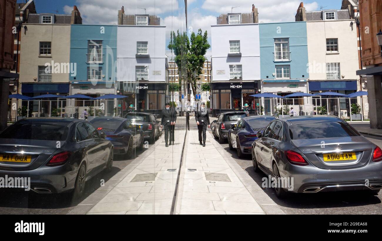 London, Greater London, England, Juni 12 2021: Spiegelbild eines Mannes, der eine Maske trägt und neben geparkten Autos einen grauen Anzug trägt. Stockfoto