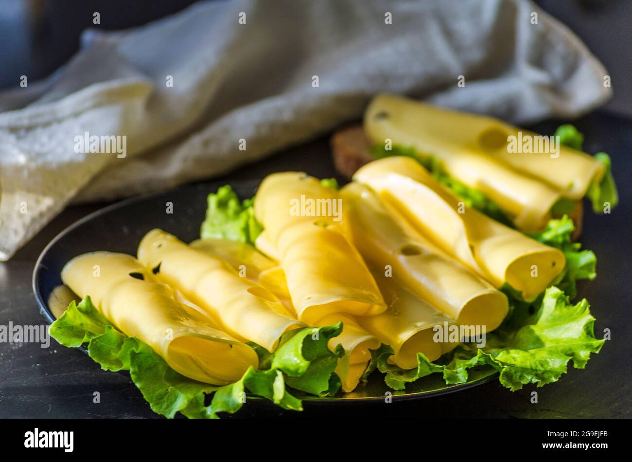 Hartkäse mit großen Löchern auf einem Teller mit Salatblättern geschnitten Stockfoto