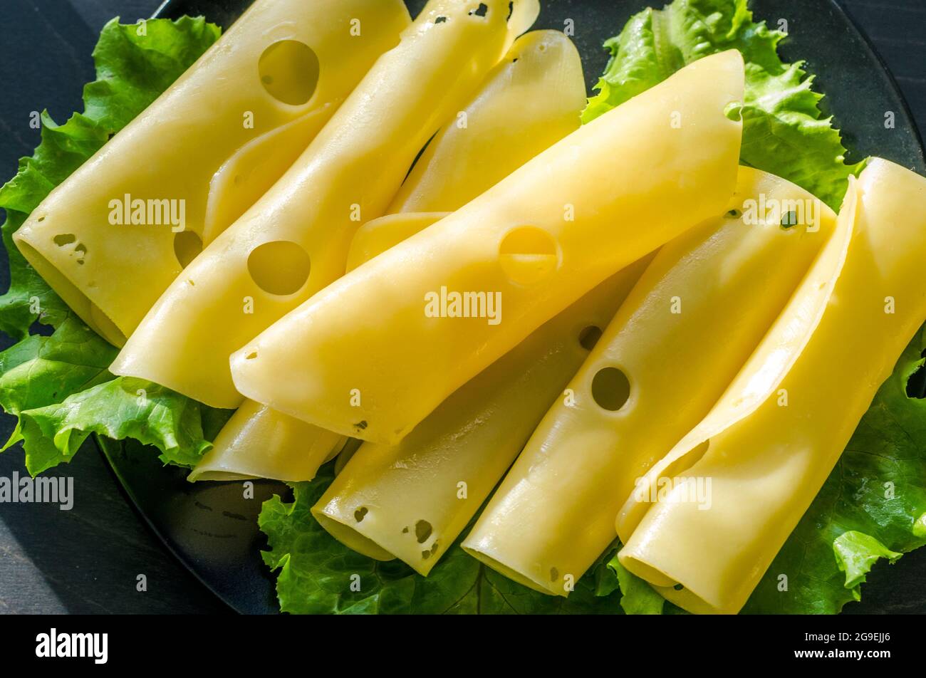 Hartkäse mit großen Löchern auf einem Teller mit Salatblättern geschnitten Stockfoto
