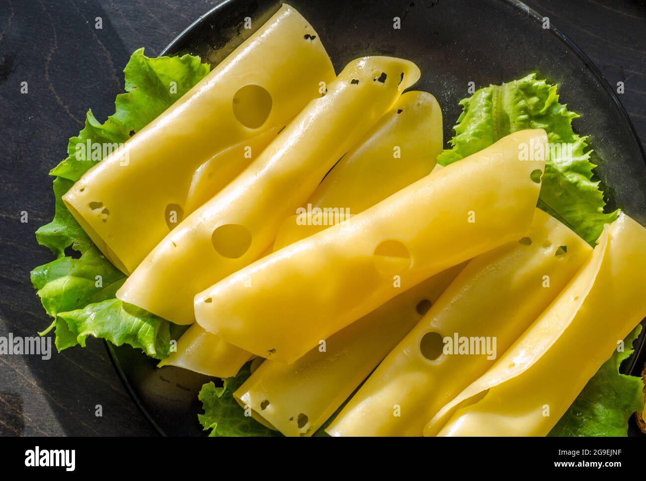 Hartkäse mit großen Löchern auf einem Teller mit Salatblättern geschnitten Stockfoto