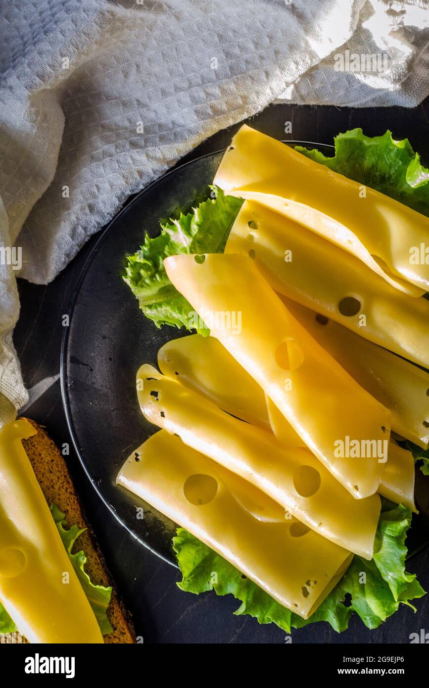 Hartkäse mit großen Löchern auf einem Teller mit Salatblättern geschnitten Stockfoto