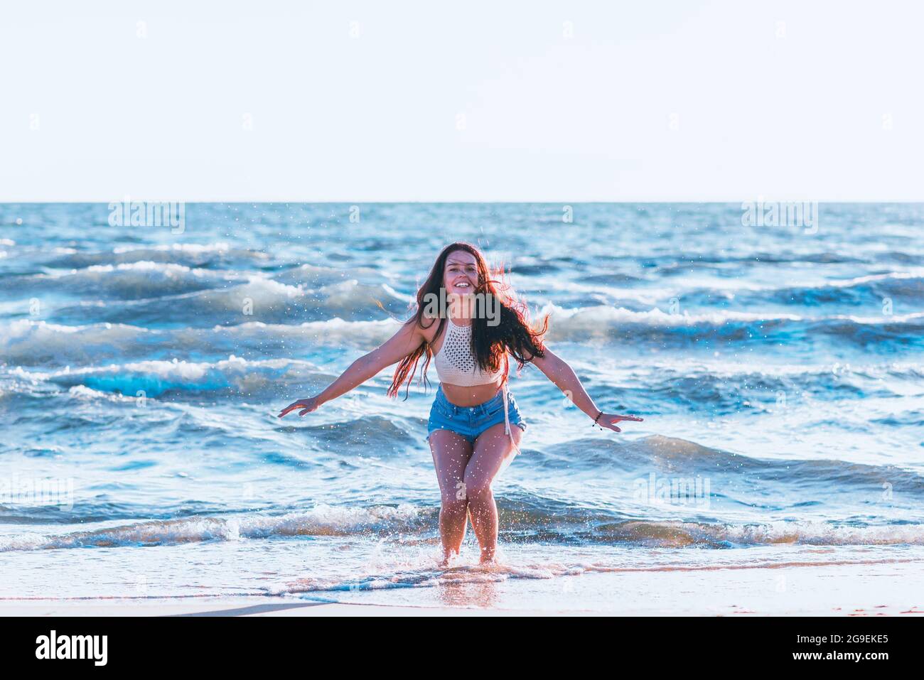 Junge Frau, die im Sommer im Meer spielt. Frau macht im Meerwasser planschen. Fröhliche junge Frau, die Spaß am Strand hat. Sie spritzt im Meereswat Stockfoto