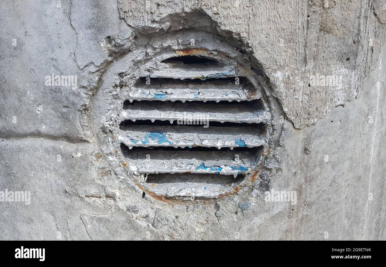 Lüftungsloch in Beton. Runder Lüftungsdeckel aus Metall für die Industrie. Rostiger und schmutziger alter runder Lüftungsrahmen mit horizontalen Metallstreifen Stockfoto