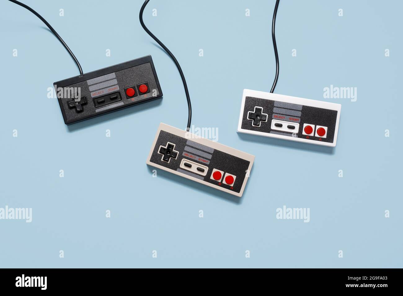 Drei Retro-Konsolen-Controller im Vintage-Stil auf einem pastellblauen Hintergrund mit Platz für Text und Text Stockfoto
