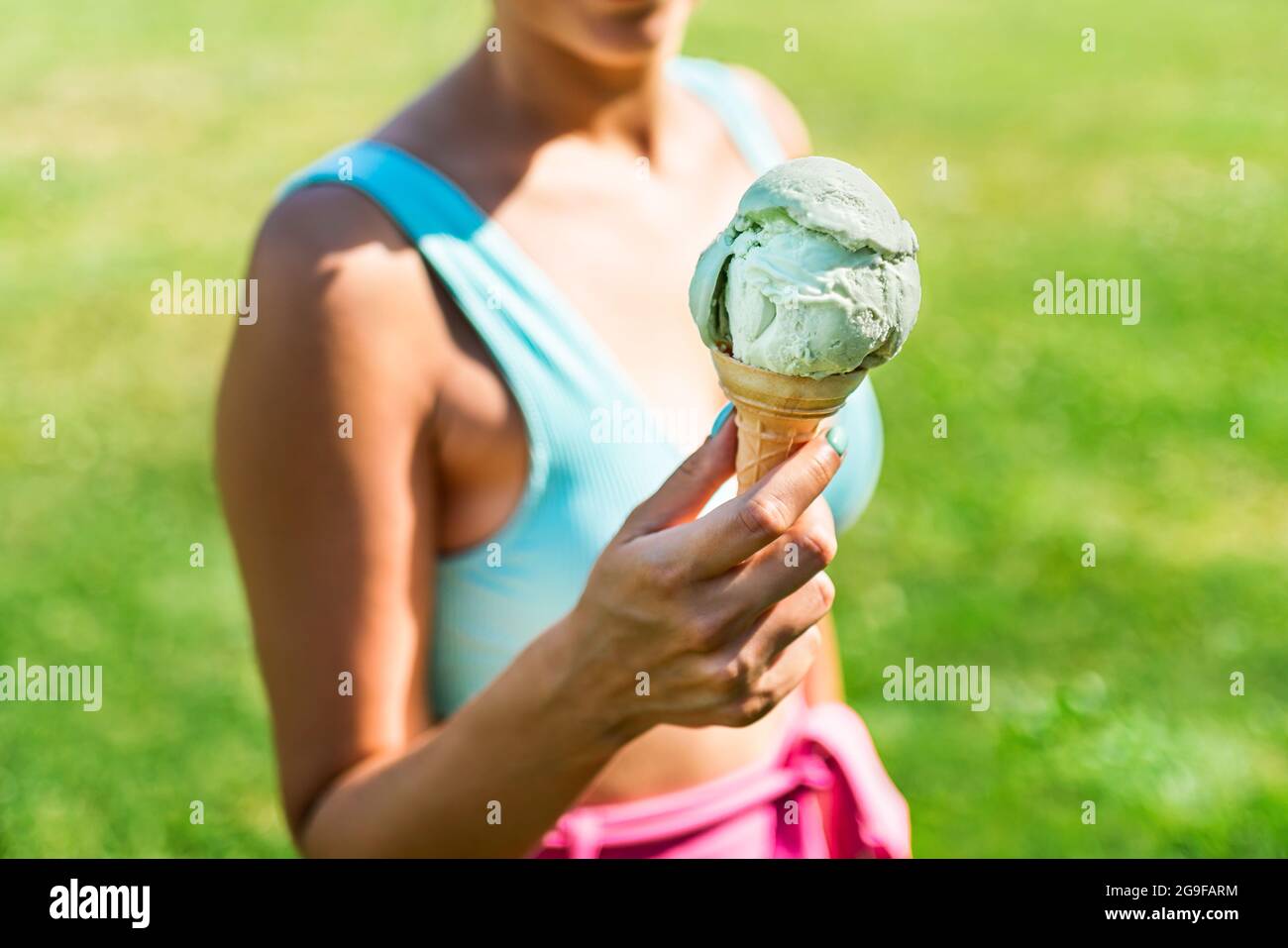 Eiskegel in der Hand einer flauen Frau im Sommer. Eiscreme und bunte Mode im Park. Retro-Vibes im Outfit und Eiscreme am sonnigen Wochenende. Stockfoto