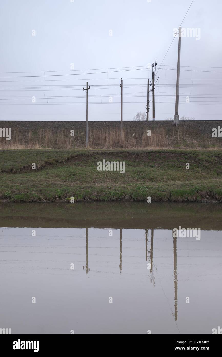 Kanal für die Entwässerung von Wasser in der Nähe einer Eisenbahnschienen. Fuzzy-Reflexion im Wasser. Stockfoto