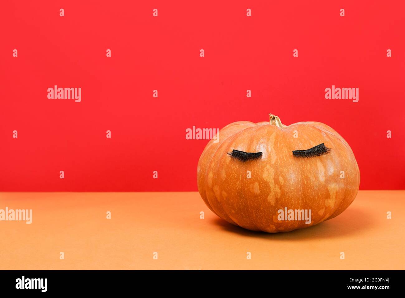 Halloween Kürbis mit falschen Wimpern auf rot. Minimaler Hintergrund des Konzepts „Weihnachtszeit“. Stockfoto