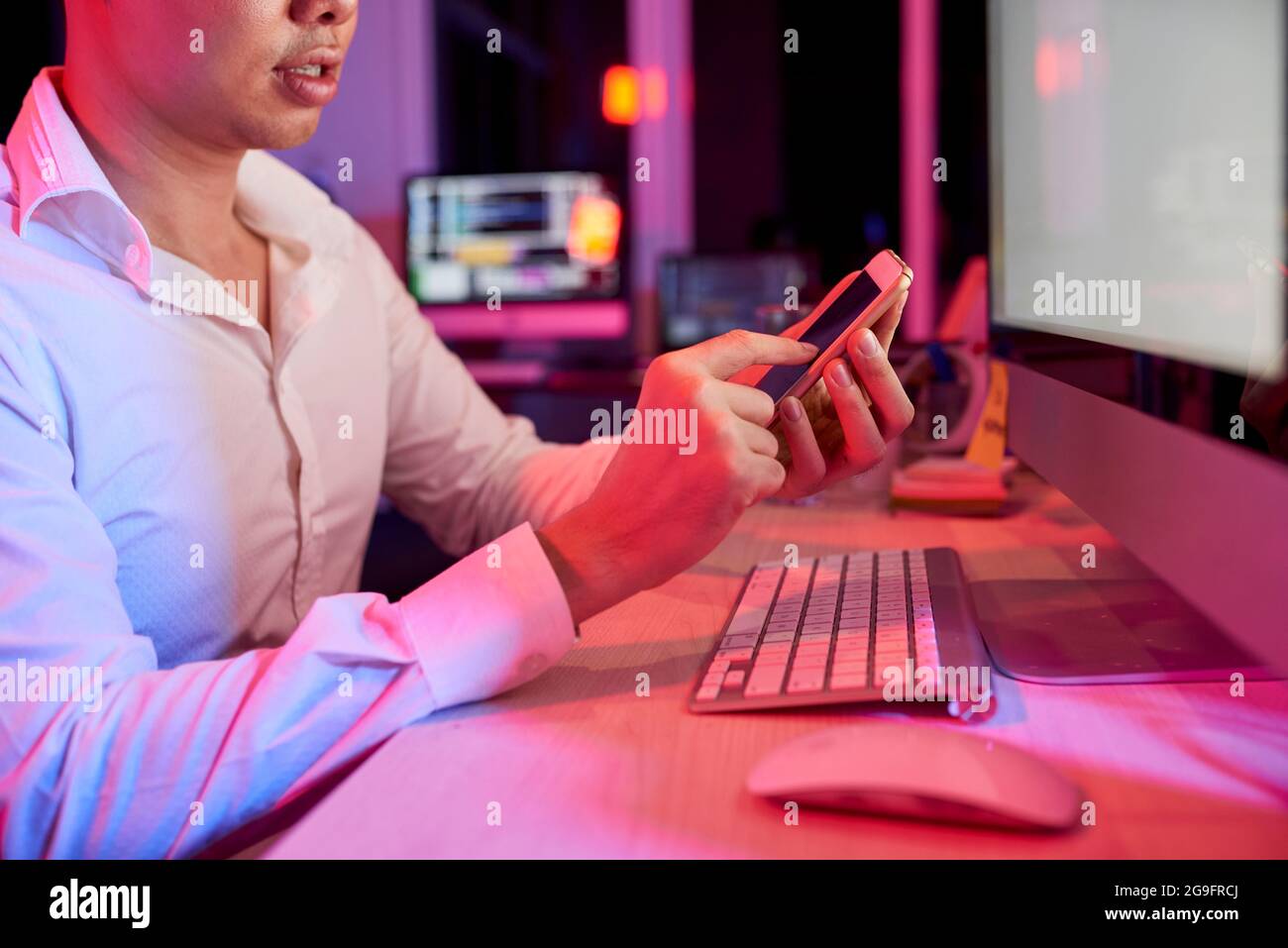 Seriöser Geschäftsmann, der am Bürotisch sitzt und SMS beantwortet oder eine mobile Anwendung verwendet Stockfoto