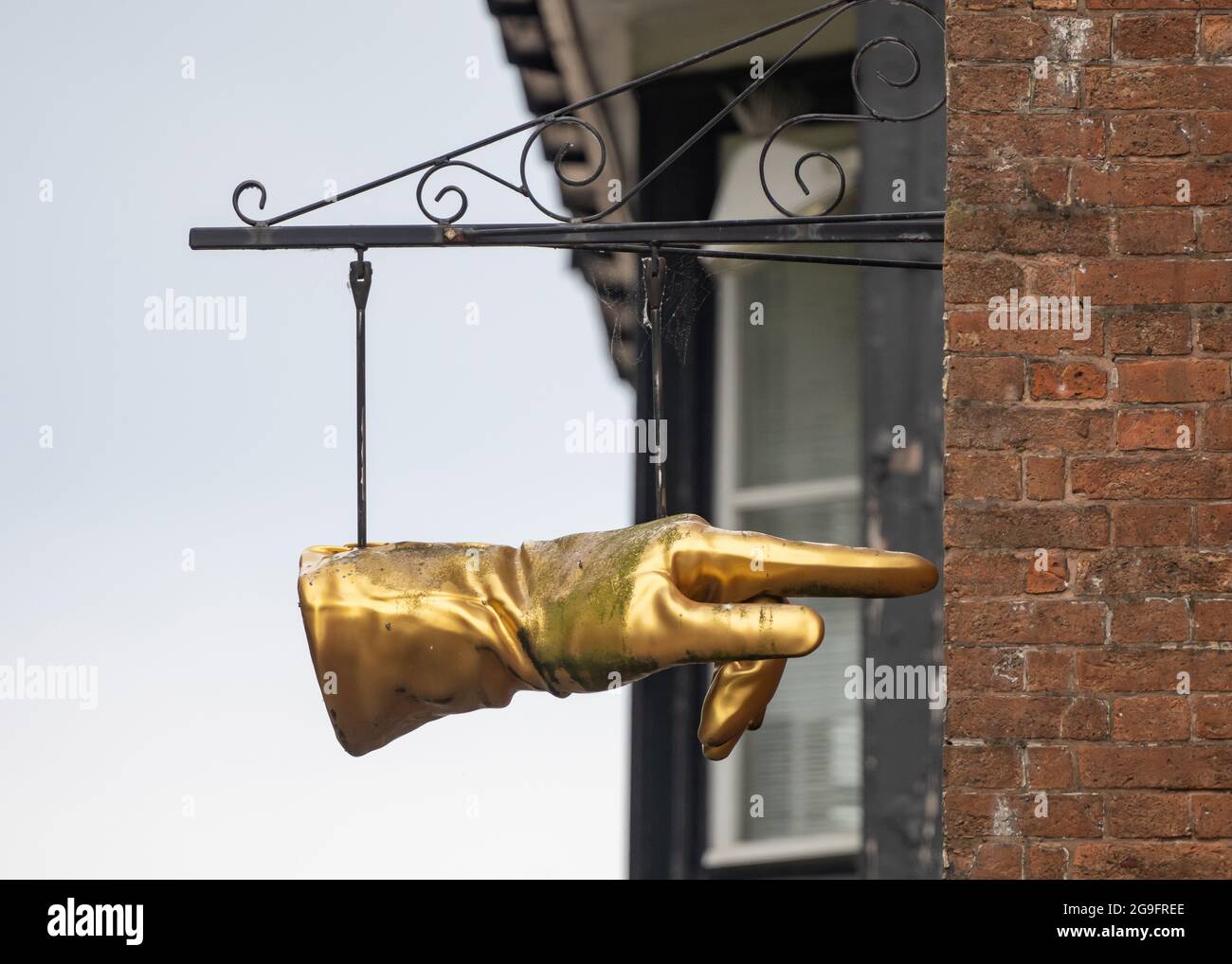 Zeigefinger goldene Handschuh Hand hängend vor Juwelier und Schmiede Shop. Vergoldet und Kunden in Richtung des Ladens in einer Gasse w Stockfoto