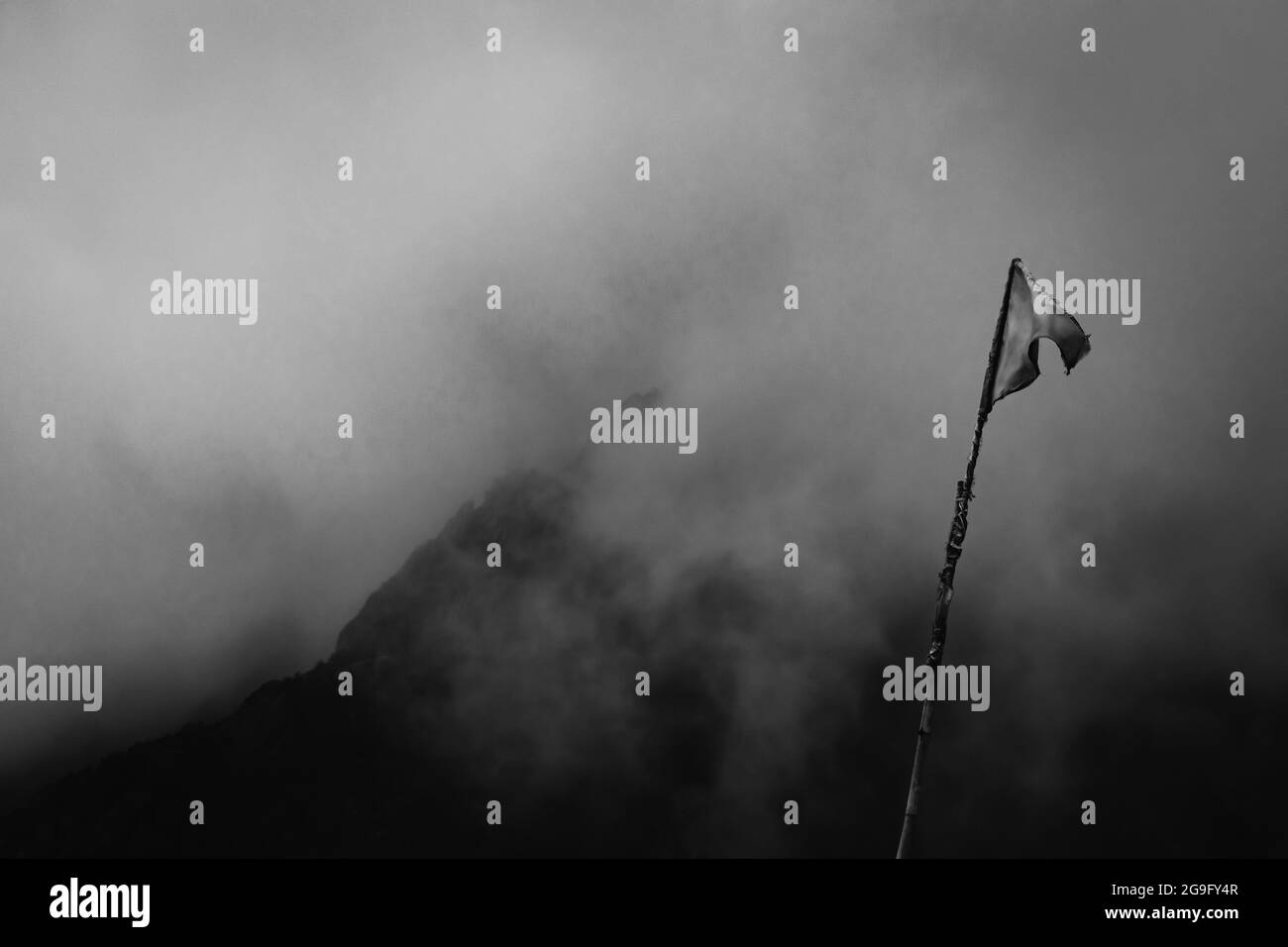 Schwarz-weiße Kunstaufnahmen einer Flagge, die in den Bergen, umgeben von Wolken, schwenkt Stockfoto
