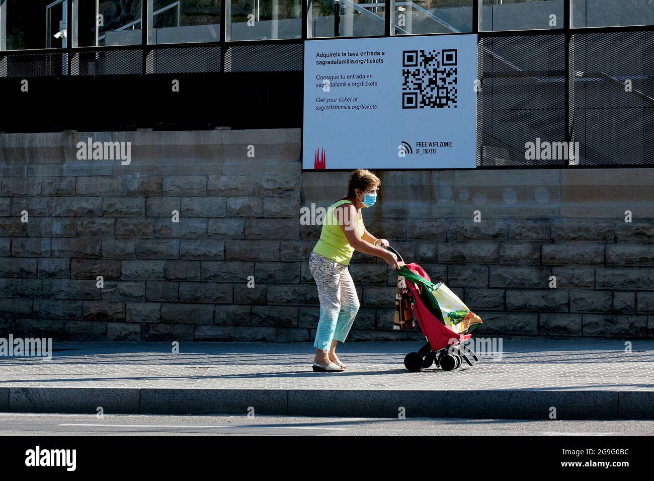 Eine Einheimische schiebt ihren Einkaufswagen an einem großen QPR-Code vorbei, der auf der Sagrada Familia in Barcelona, Spanien, angebracht ist. Stockfoto