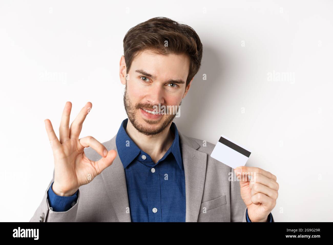 Einkaufen. Schöner Mann zeigt okay Zeichen und Kunststoff-Kreditkarte, alles unter Kontrolle, keine Sorgen Geste, weißer Hintergrund Stockfoto