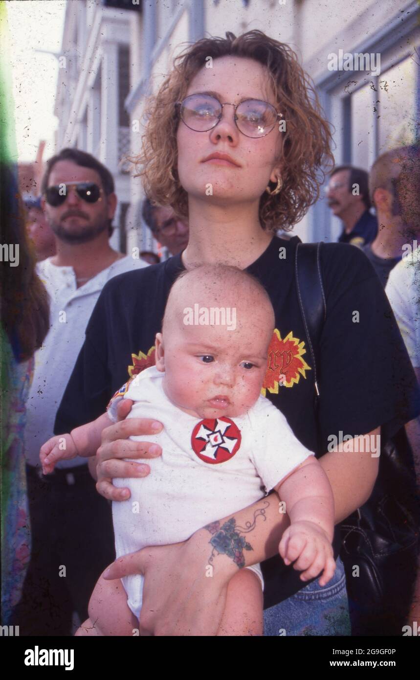 Houston Texas USA, Juli 1990: Mutter trägt ein Kleinkind, das einen Einteiler mit einem Ku Klux Klan-Abzeichen trägt, während sie während des G7-Gipfels eine KKK-Kundgebung durch die Innenstadt beobachten. ©Bob Daemmrich Stockfoto