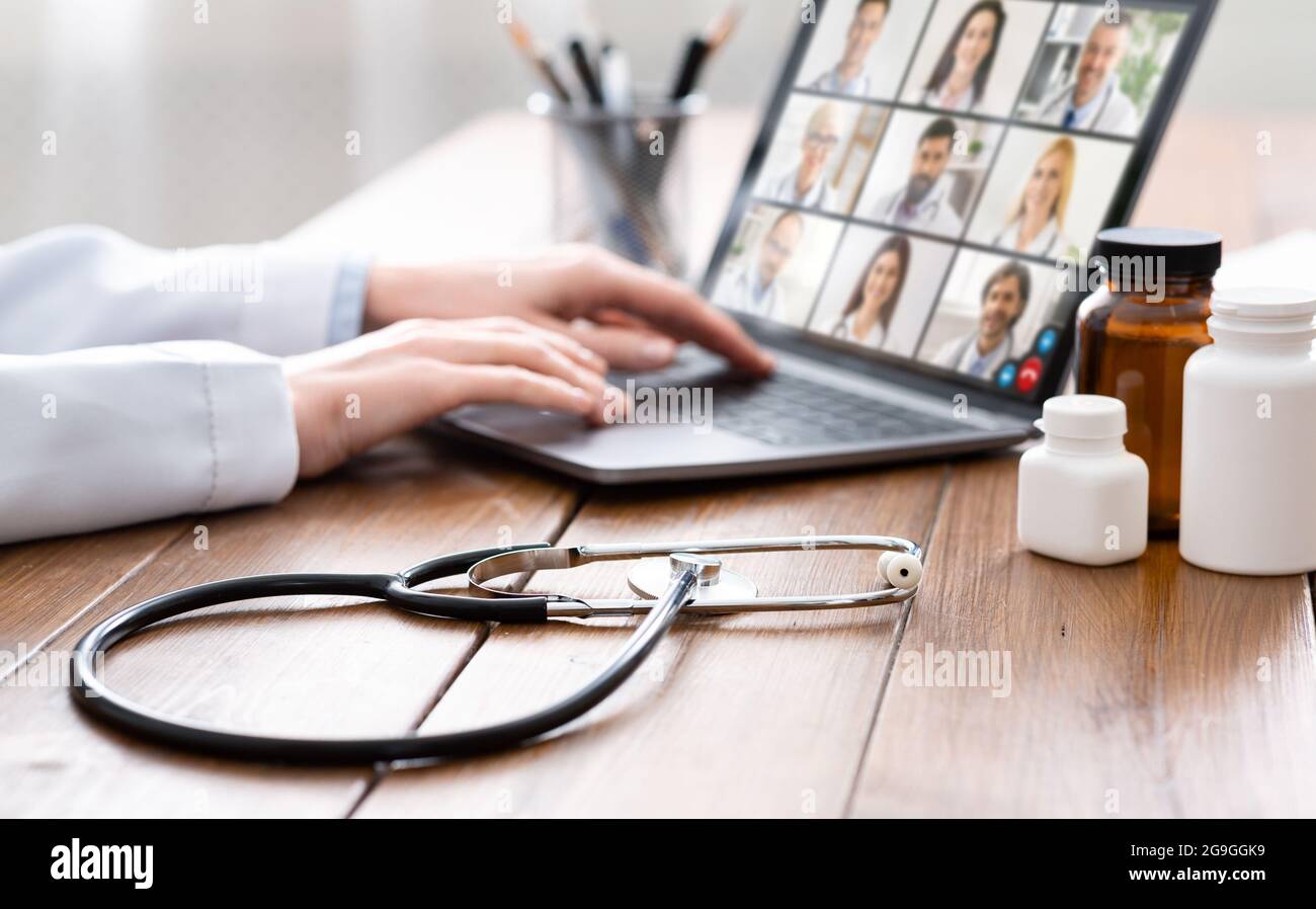 Ärztin im weißen Mantel mit Laptop und Video-Chat mit einem Ärzteteam am Arbeitsplatz im Büro. Selektiver Fokus auf Stethoskop und medizinisches p Stockfoto