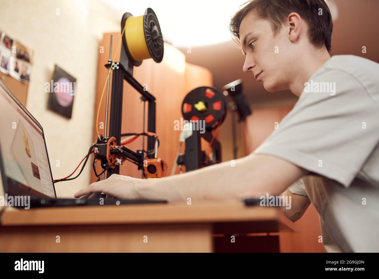 Niedriger Winkel des konzentrierten jungen Mannes, der 3D-Modell auf dem Laptop durchstöbert, bevor er am Tisch sitzt und im Studio arbeitet Stockfoto