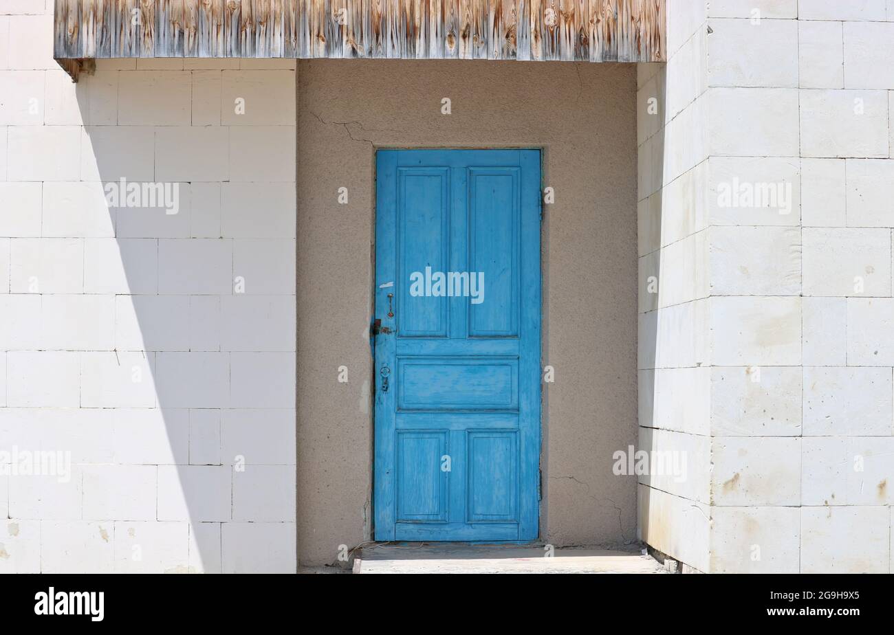 Ältere blaue Tür in einer weißen Wand. Die Wand besteht aus hellen Steinblöcken. Stockfoto