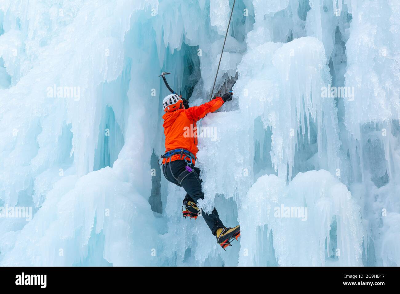 Athlet klettert mit Eis bedeckte Klippe, benutzt Eispickel und piercingst vordere Steigeisen direkt auf das Eis Stockfoto