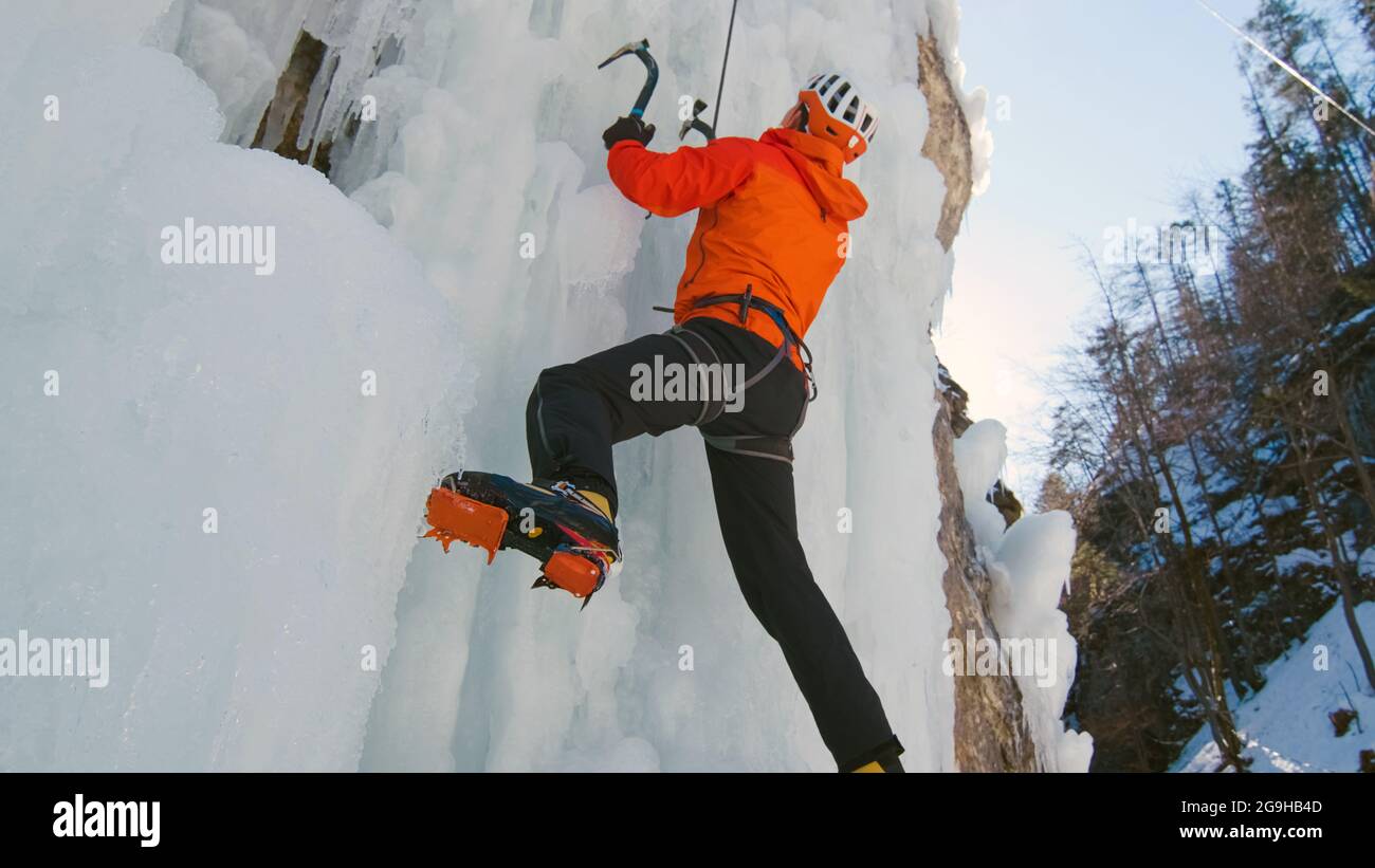 Mann klettert auf einem gefrorenen Wasserfall, indem er mit Steigeisen ins Eis tritt und auf das Eis drückt Stockfoto