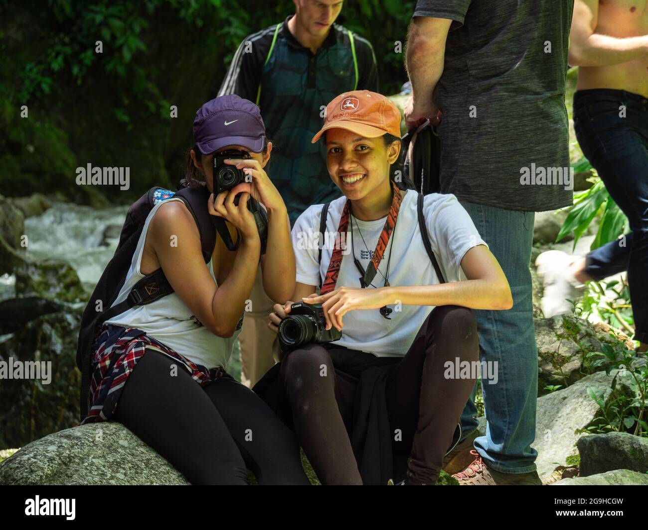 Amada, Antioquia, Kolumbien - Juli 18 2021: Hispanische Frauen sitzen auf Felsen am Flussufer und machen Fotos mitten in der Natur Stockfoto