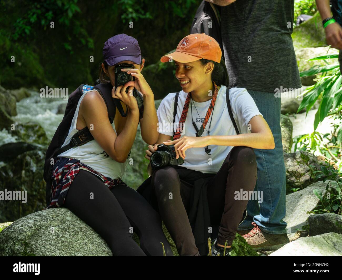 Amada, Antioquia, Kolumbien - Juli 18 2021: Hispanische Frauen sitzen auf Felsen am Flussufer und machen Fotos mitten in der Natur Stockfoto