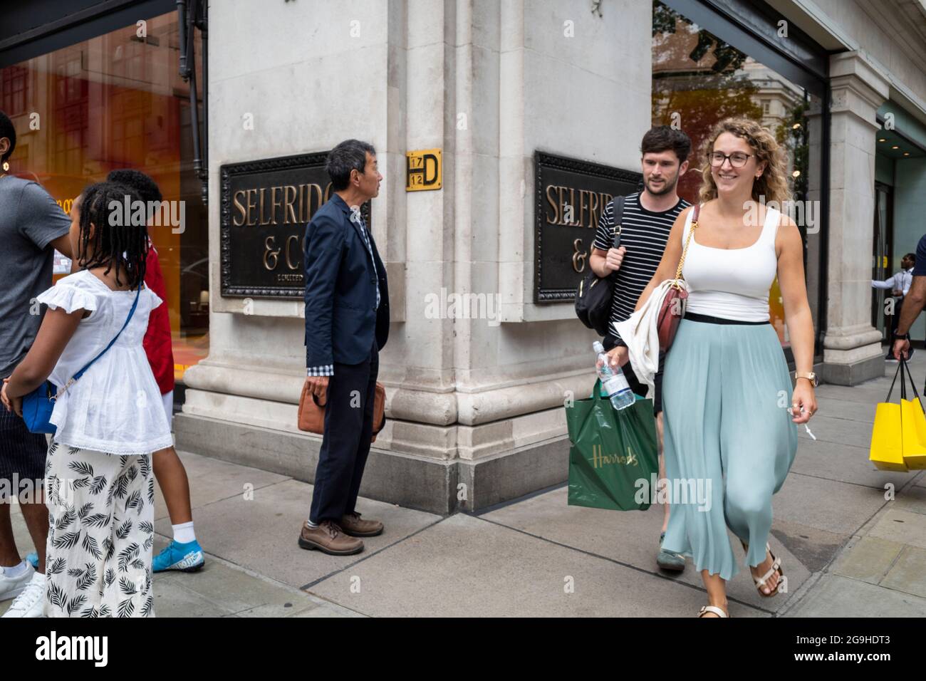 London, Großbritannien. 26. Juli 2021. An der Außenseite des Flaggschiff-Kaufhauses Selfridge in der Oxford Street passieren Menschen die Beschilderung. Die Kaufhauskette wurde von ihren Besitzern, der Familie Weston, zum Verkauf angeboten. Die Berater der Credit Suisse führen den Verkauf an und hoffen, bis Ende des Jahres einen Deal abzuschließen, der sich auf bis zu 4 Mrd. £belaufen könnte, was dem Bericht zufolge eher das Immobilienportfolio als das zugrunde liegende Geschäft widerspiegelt, das während der Coronavirus-Pandemie zu kämpfen hatte. Kredit: Stephen Chung / Alamy Live Nachrichten Stockfoto