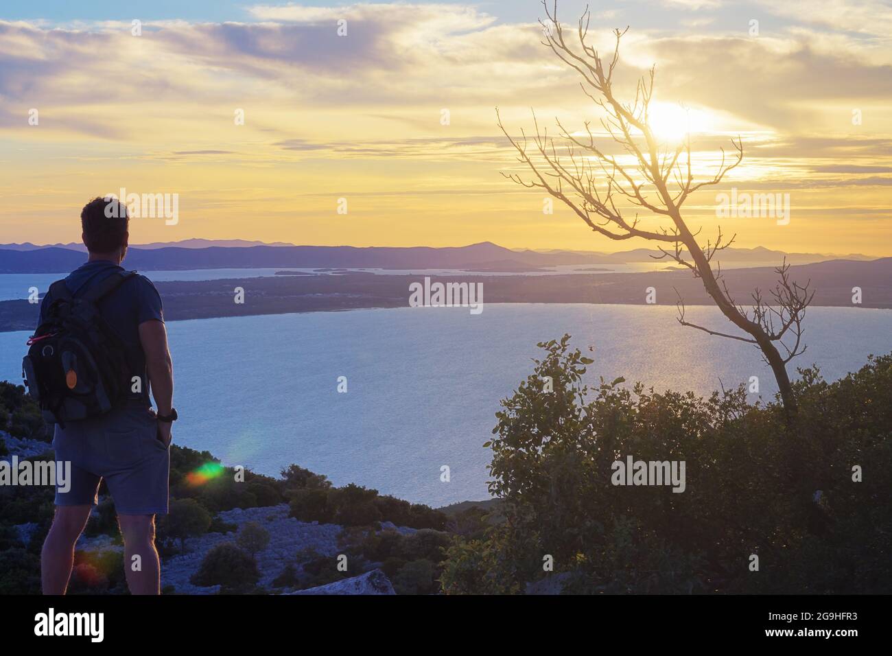 Männlicher Wanderer auf dem Hügel, der einen wunderschönen Sonnenuntergang über der Adria beobachtet. Konzepte für Wandern, Leistung, Erwartung, Optimismus und Selbstreflexion. Stockfoto