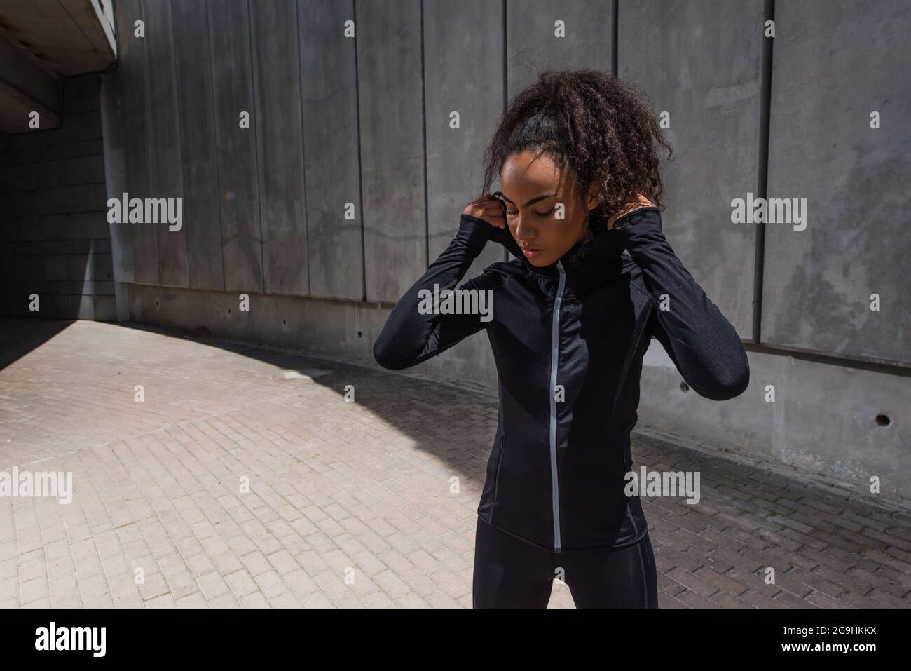 afroamerikanische Sportlerin, die die Kapuze der Sportjacke im Freien verstellt Stockfoto