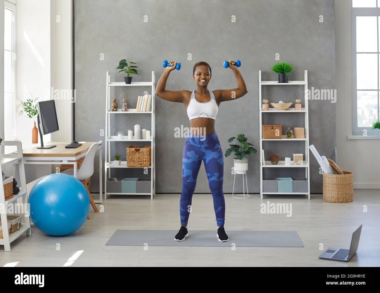 Glückliche junge schwarze Frau im aktiven Ohr mit Fitness-Training mit Hanteln zu Hause Stockfoto