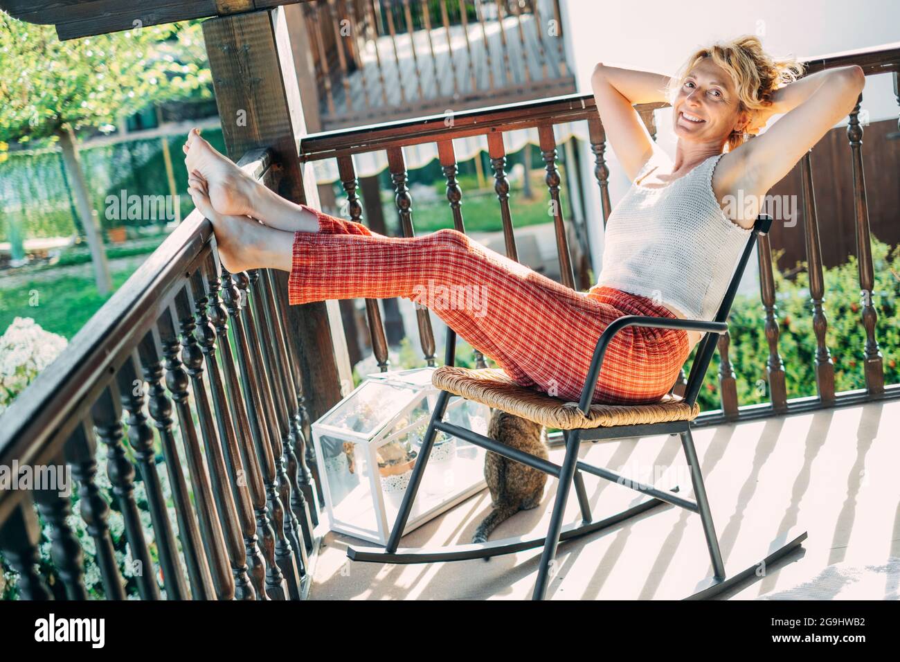 Porträt einer jungen reifen kaukasischen blonden Frau, die sich zu Hause auf der Veranda entspannt und in einem Schaukelstuhl sitzt. Lifestyle-Konzept. Stockfoto