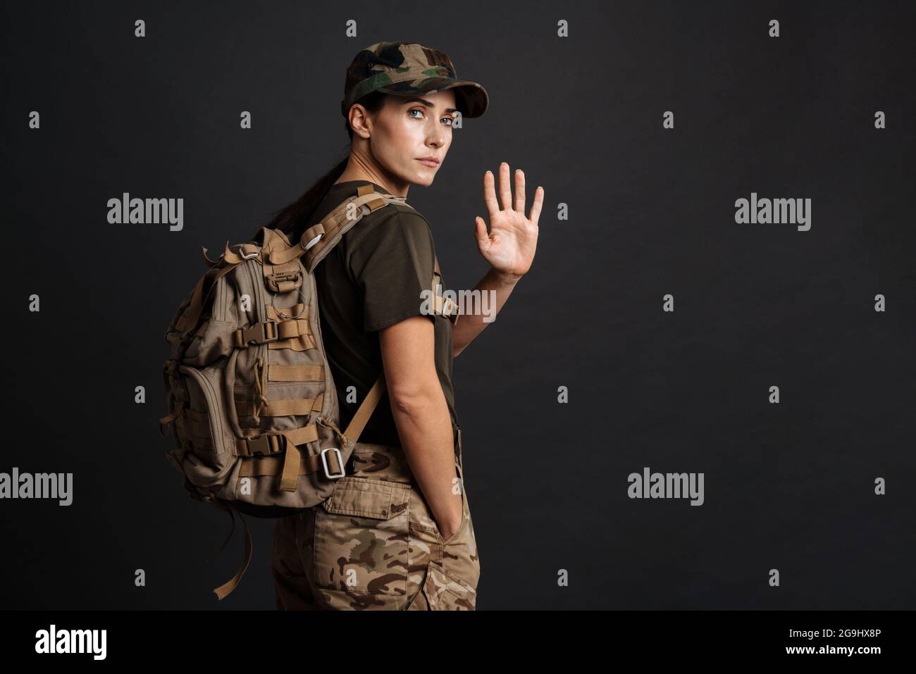 Ernst schöne Soldatin Frau mit Armee Rucksack winkende Hand isoliert auf schwarzem Hintergrund Stockfoto