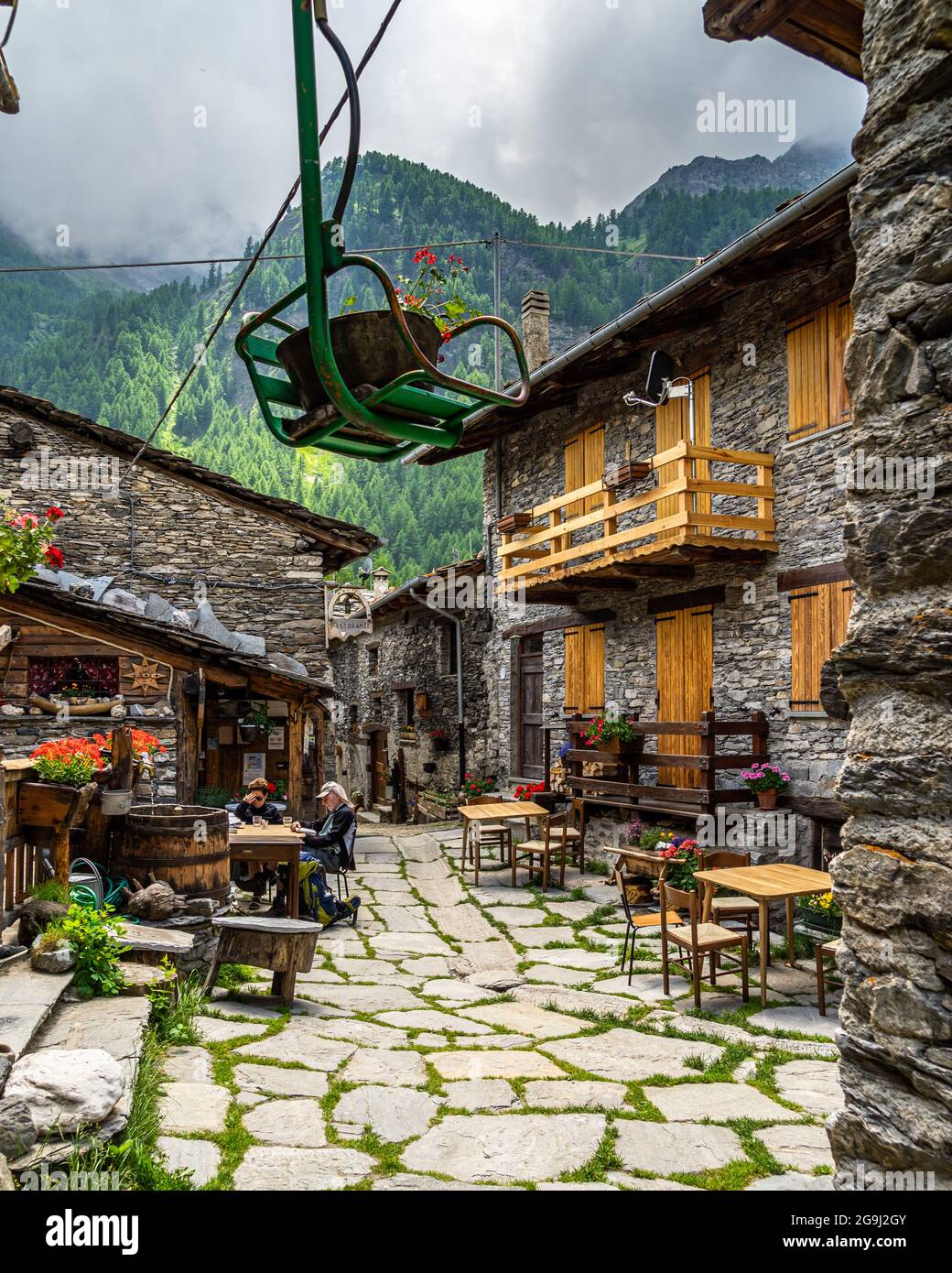Chianale, Piemont, Italien, Juni 2021 – Dekoratives Sessellift-Modell, das zwischen den typischen alpinen Gebäuden hängt. Stockfoto