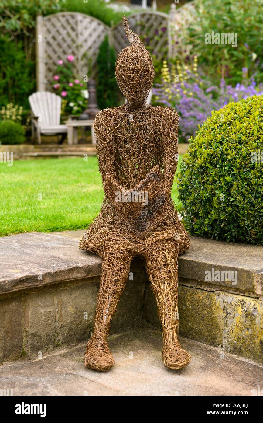 Willow Skulptur Kunst des Mädchens (ornamental Feature) in einem wunderschönen Landschaftsgarten (blühende Pflanzen, Kastenball, Rasen, Sitz) - Yorkshire, England UK. Stockfoto