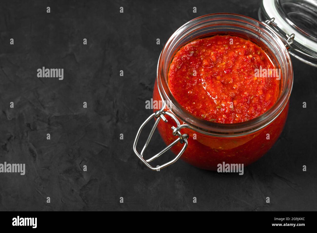 Harissa-Sauce. Adjika. Scharfe Chilischote-Sauce in einem Glas auf schwarzem Hintergrund aus nächster Nähe. Tunesische, georgische und arabische Küche. Speicherplatz kopieren. Stockfoto