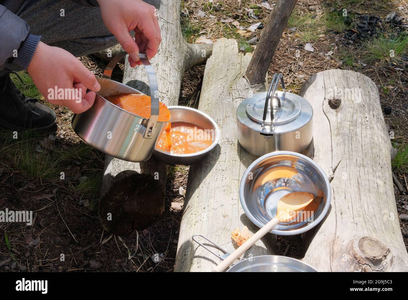 Touristische Küche bei Aktivitäten im Freien. Suppe in Schüsseln auf Holzstämmen im Wald. Camping Lebensmittelherstellung. Stockfoto