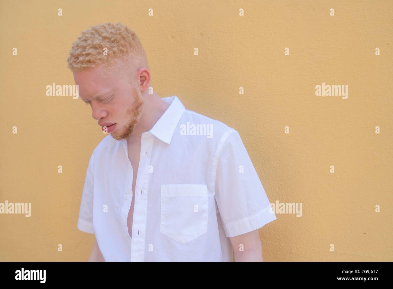 Deutschland, Köln, Albino Mann in weißem Hemd an gelber Wand Stockfoto