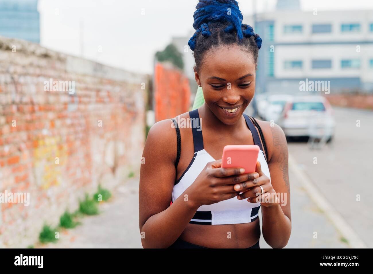 Italien, Mailand, lächelnde Frau in Sportkleidung, die in der Stadt auf das Smartphone schaut Stockfoto