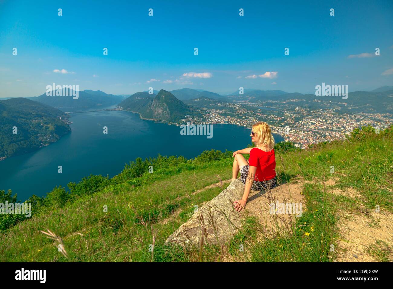 Frau, die auf der Schweizer Stadt Lugano am Lugano-See in der Schweiz sitzt. Luftaussicht vom Monte Bre Mount. Lugano Stadtbild mit San Salvatore Stockfoto