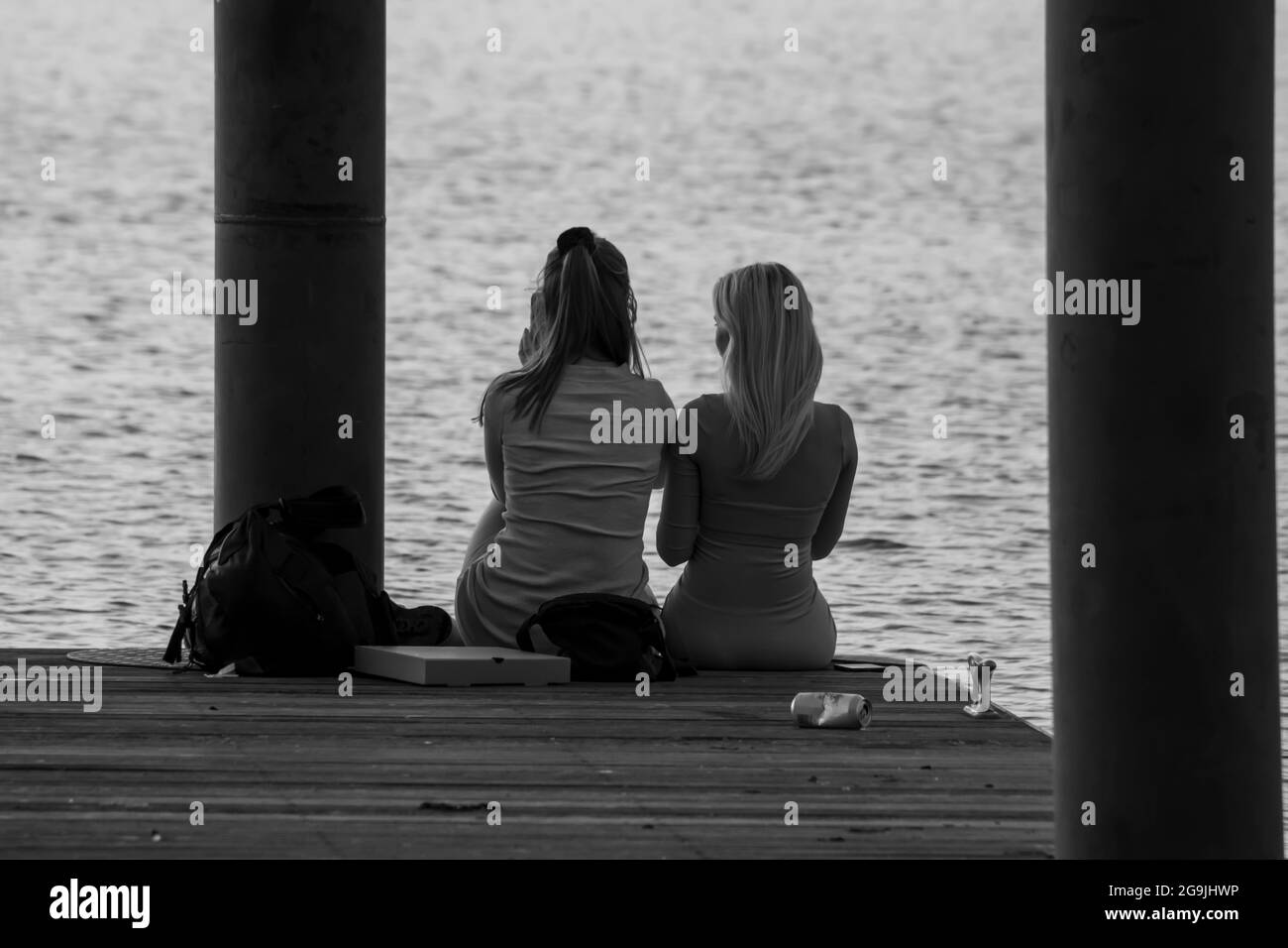 2 Freunde saßen am Rande eines Ponton mit Blick auf Lake Windermere bei Sonnenuntergang Stockfoto