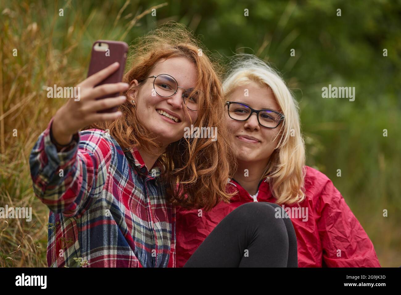 Mädchen, die Selfies mit einem Smartphone machen, treten in natürlicher Umgebung auf, konzentrieren sich auf das Gesicht auf der linken Seite Stockfoto